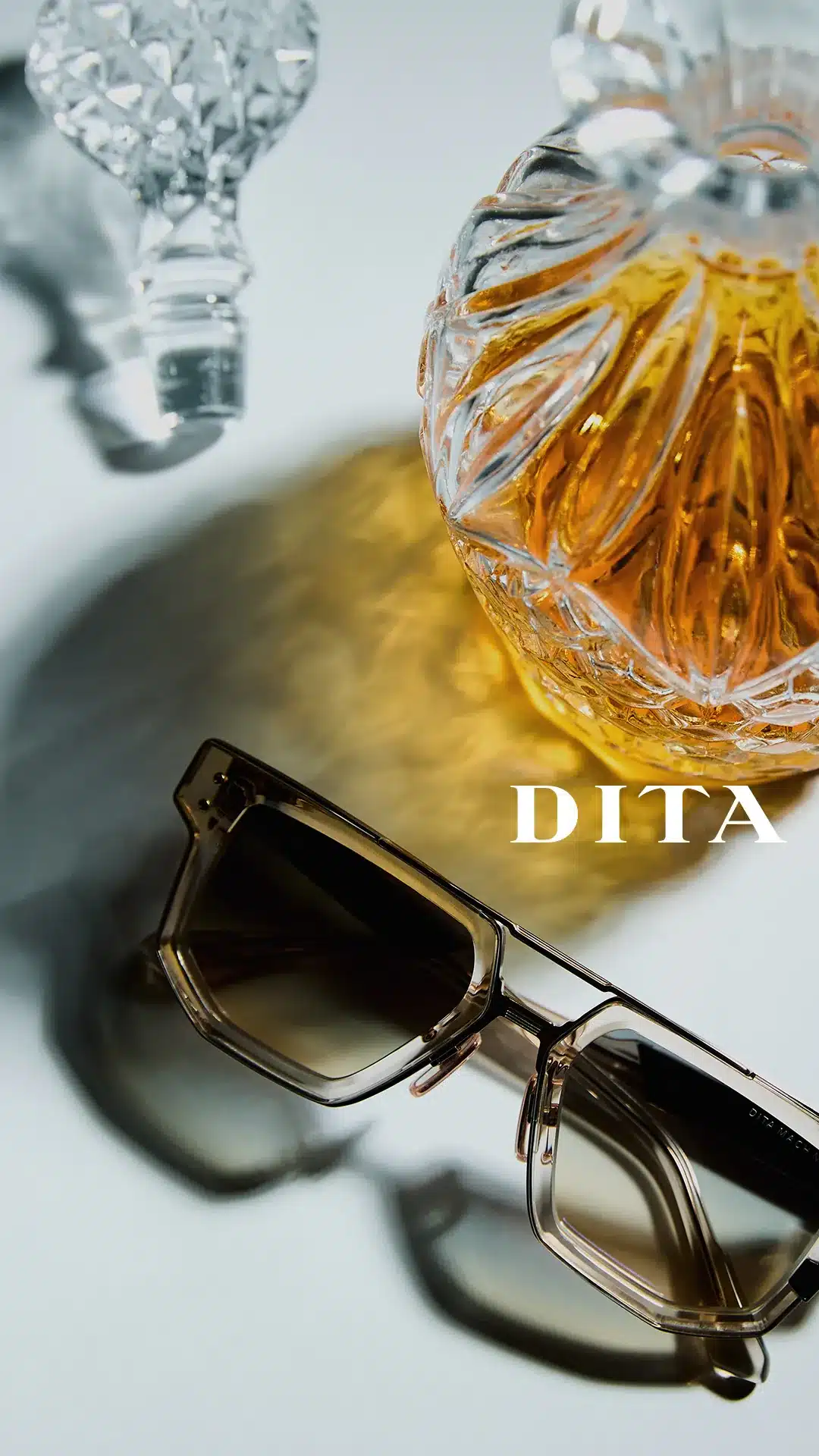DITA crystal acetate and titanium sunglasses beside a cut-glass decanter