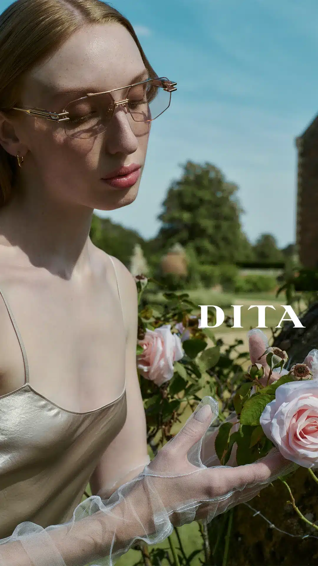 Model in DITA rose-gold rimless optical frames beside a pink rose bush
