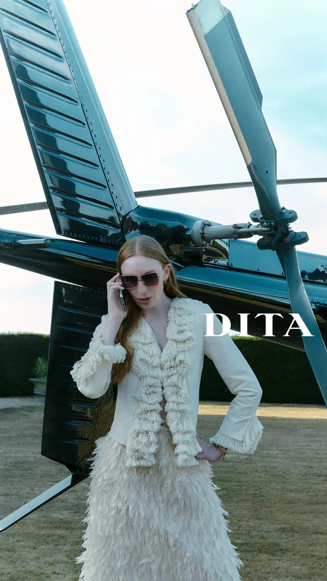 Model in DITA oversized gold sunglasses standing in front of a black helicopter