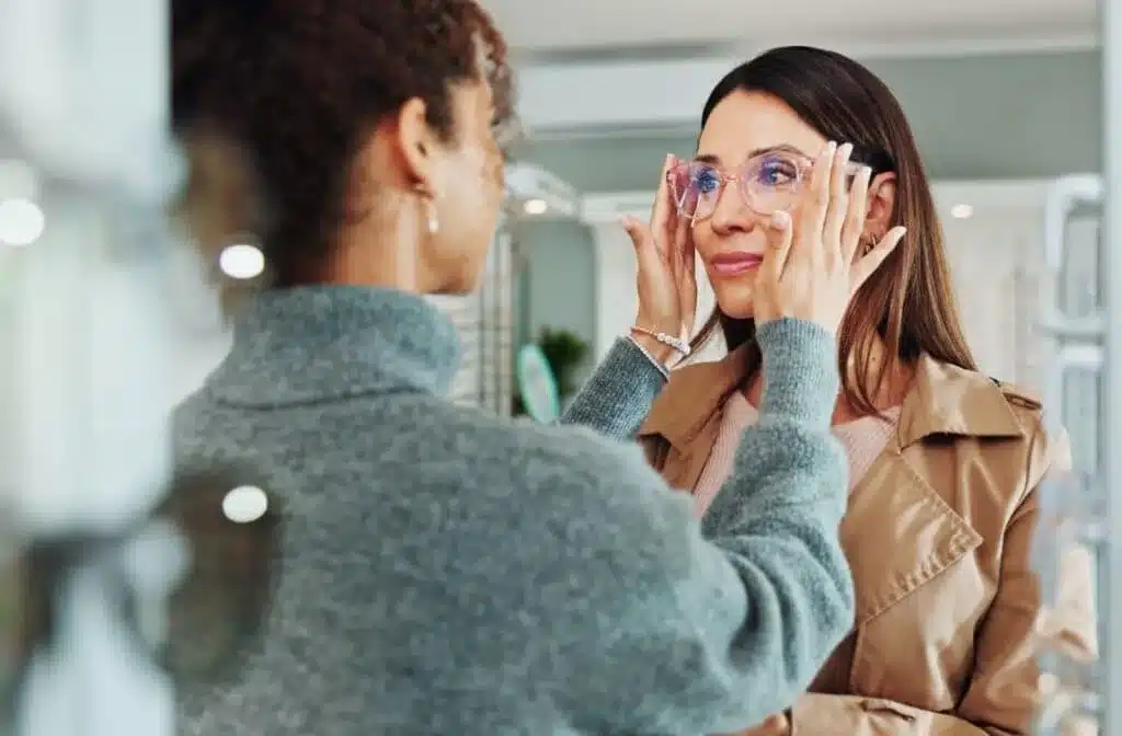 Woman wearing pink-tinted eyeglasses with hands near the frame during a fit check